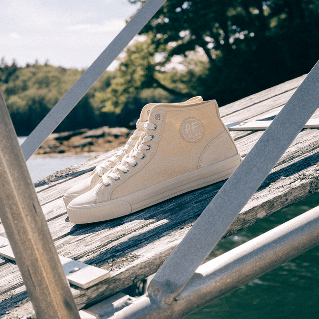 Beige high-top sneakers on wooden ramp by a body of water.