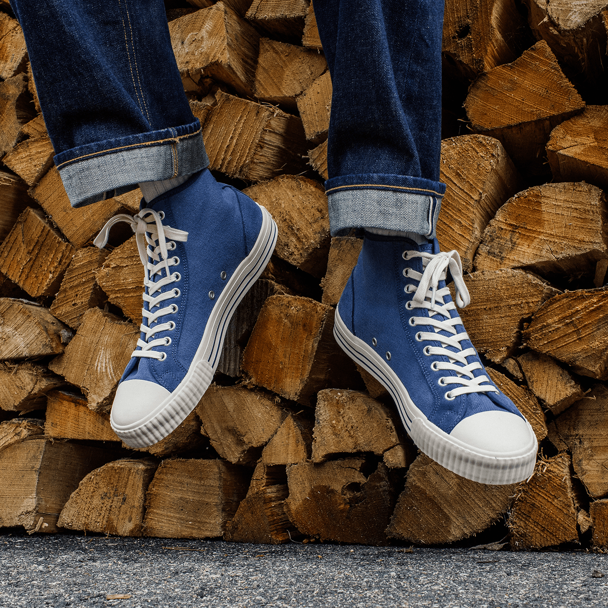 Person wearing blue high-top sneakers with white soles while sitting on a pile of firewood.