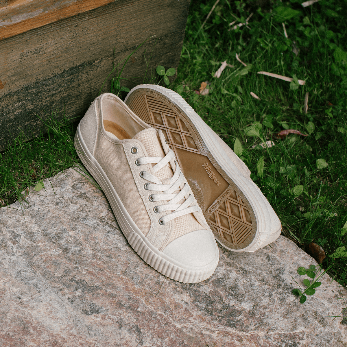 Pair of beige low-top sneakers on a stone with grass in the background.