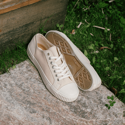 Pair of beige low-top sneakers on a stone with grass in the background.