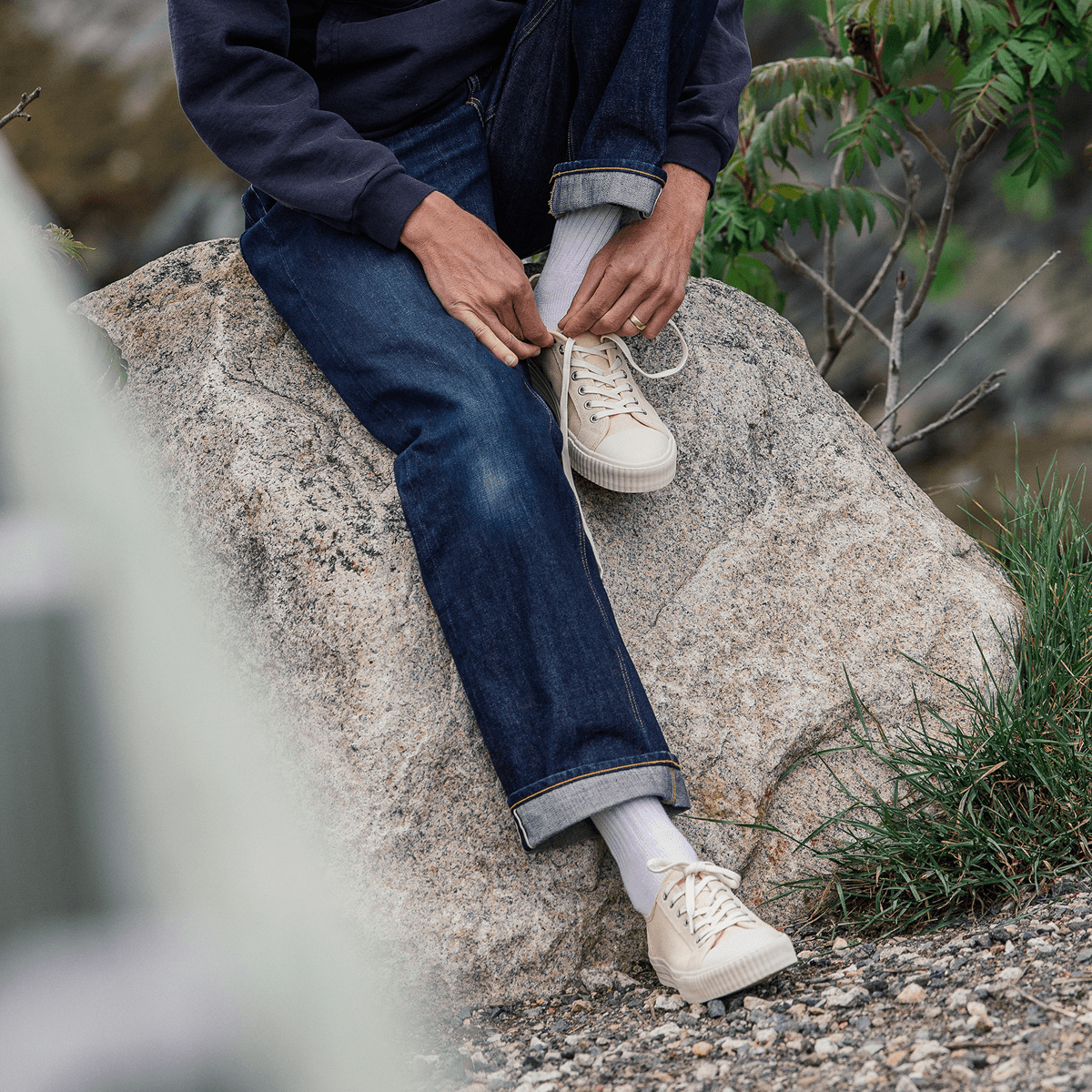 Person sitting on a boulder wearing blue jeans and beige low-top sneakers.