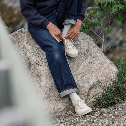 Person sitting on a boulder wearing blue jeans and beige low-top sneakers.