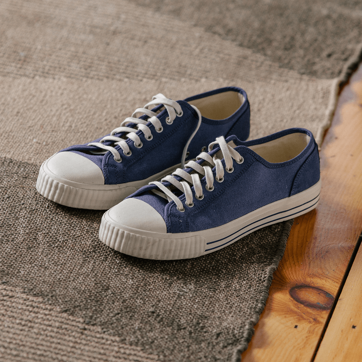 Pair of blue low-top sneakers with white soles on a rug.