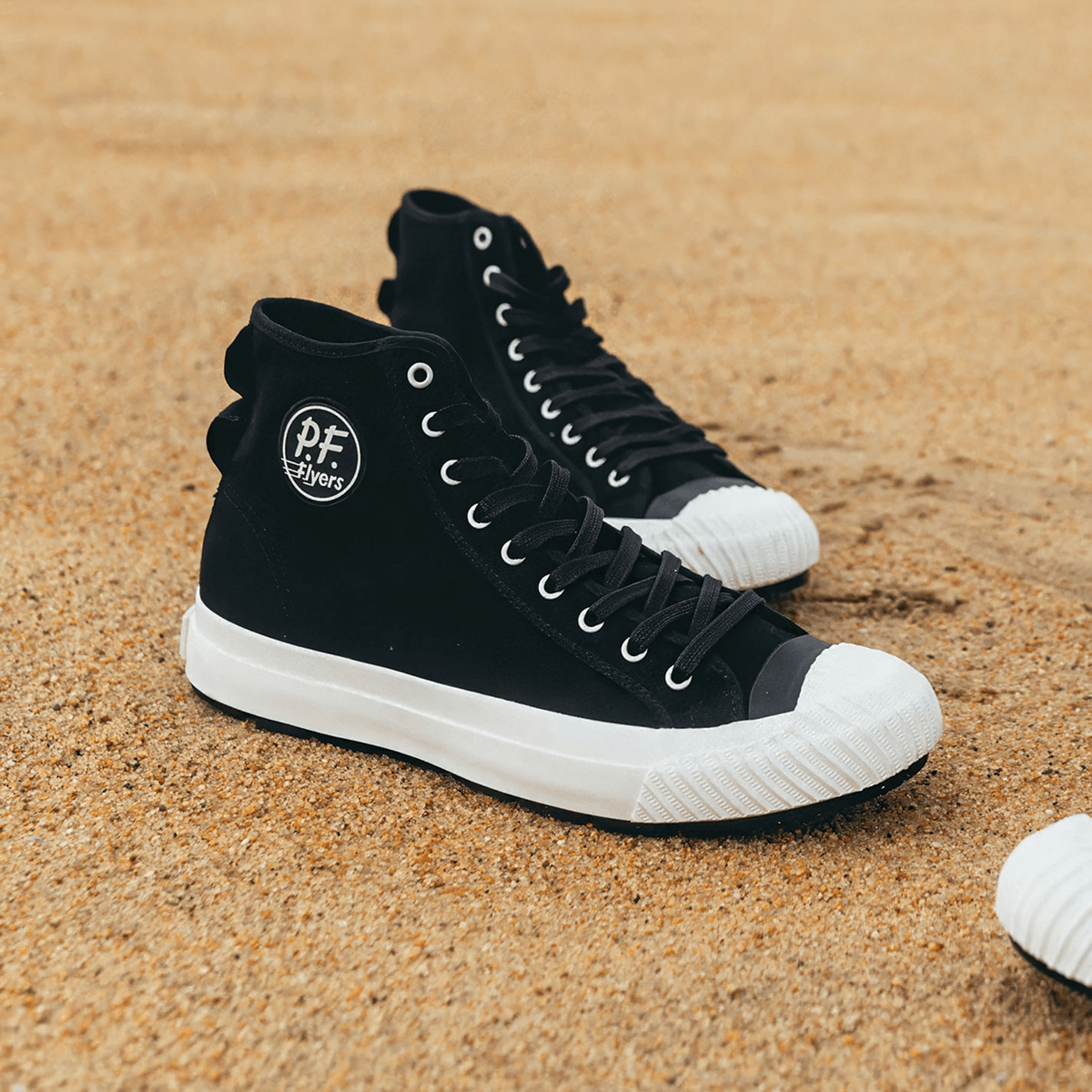 Black high-top sneakers with white soles on sand.