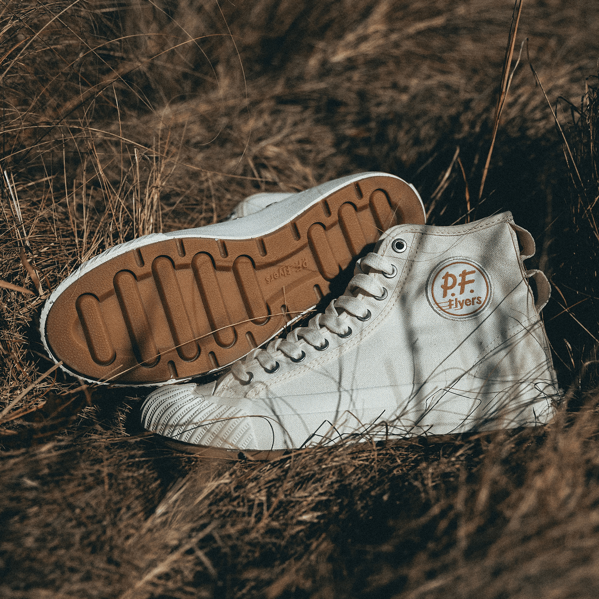 White high-top sneakers with brown soles resting on dry grass.