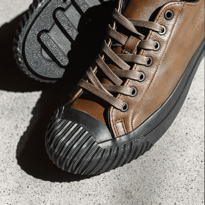 Close up of brown leather low-top sneakers with black soles on a concrete floor.