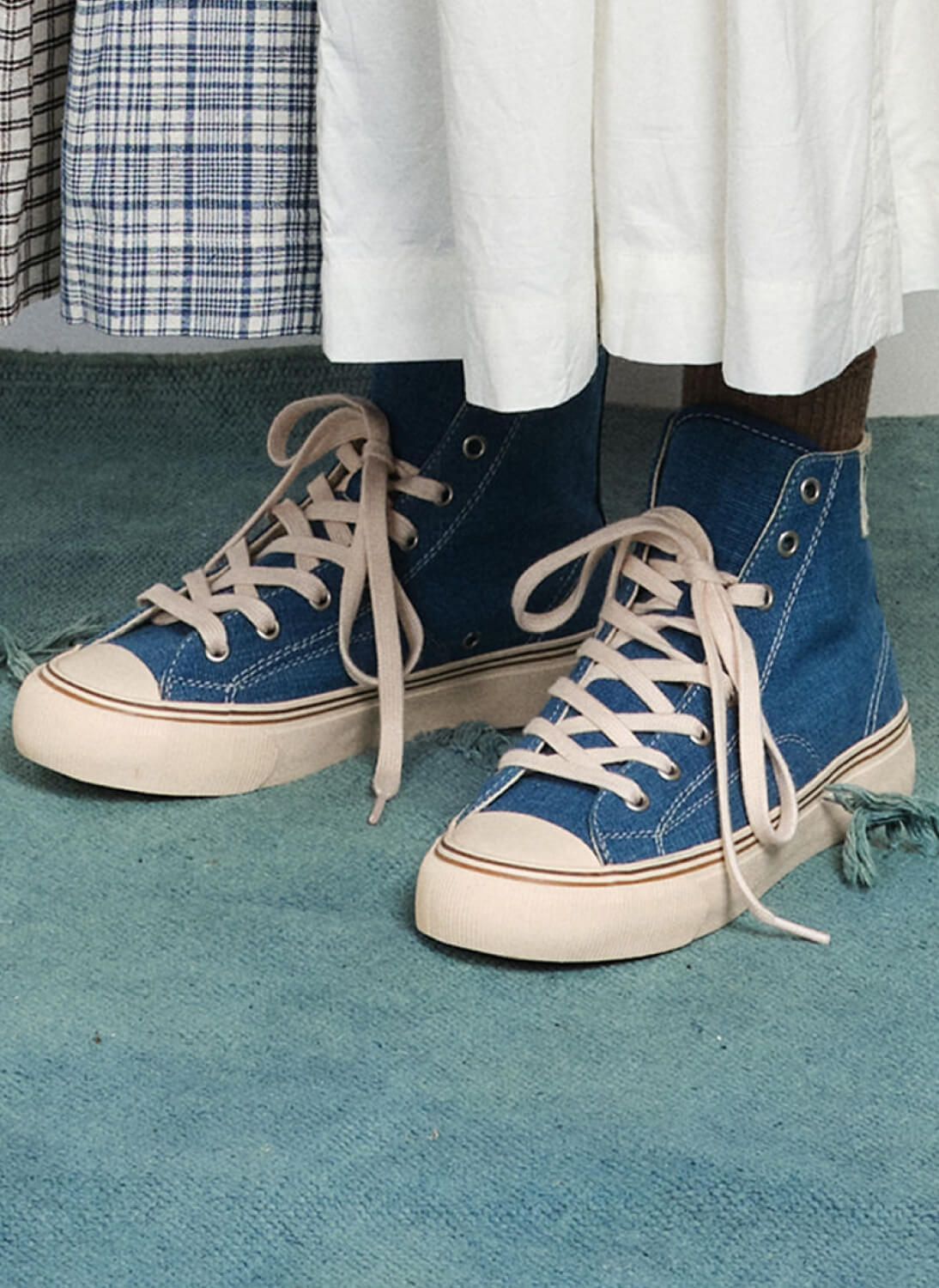 A person standing on a rug wearing indigo high-top sneakers.