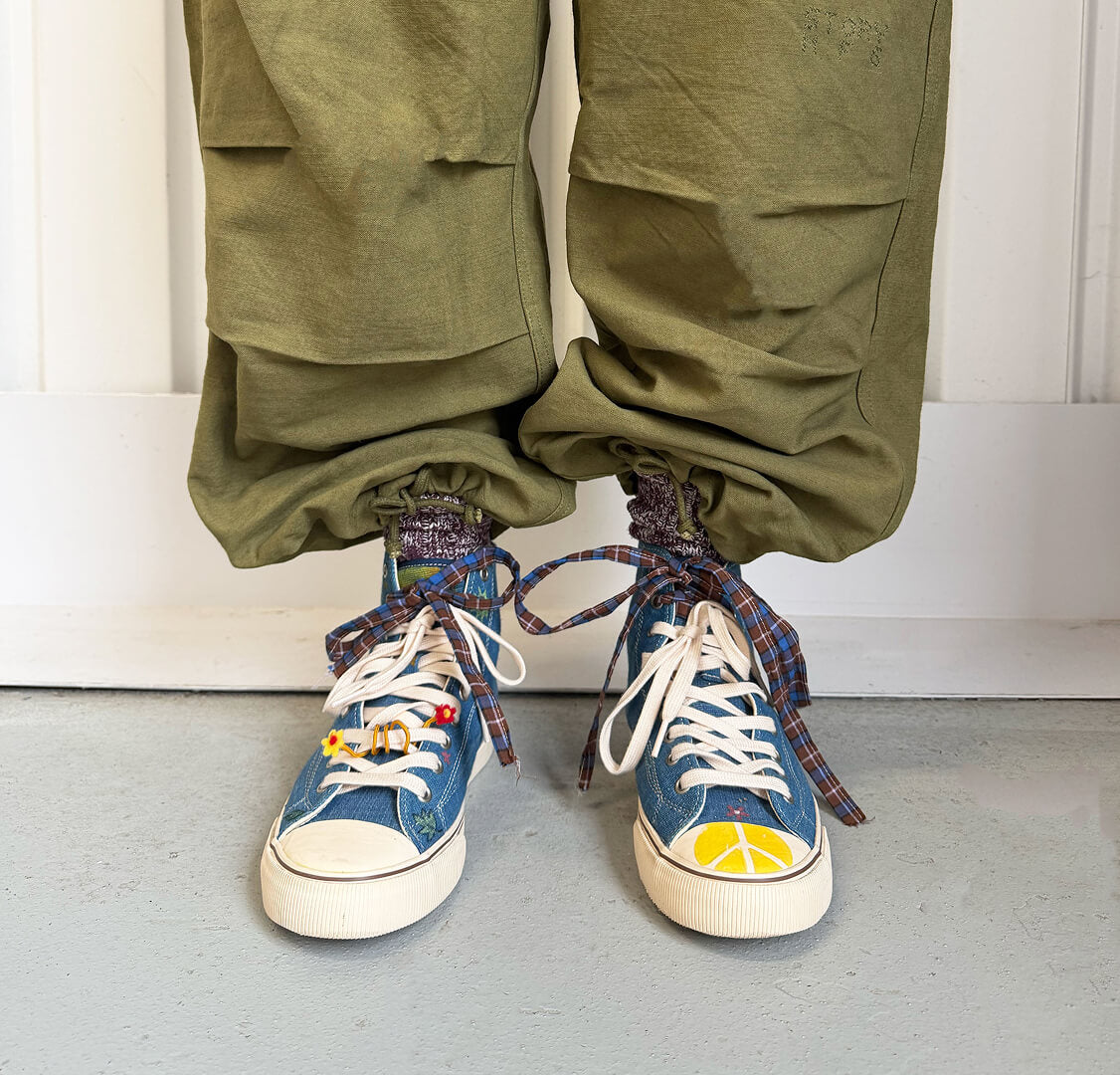 A person standing against a white paneled wall wearing indigo high-top sneakers.
