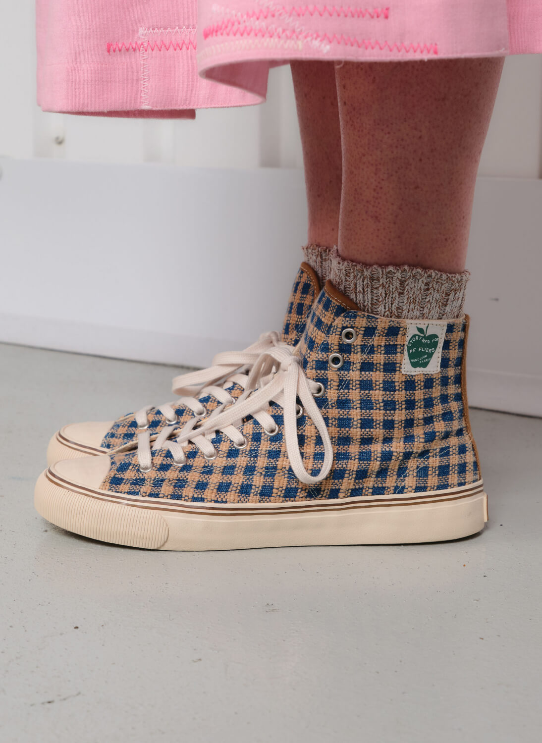 Close-up of a person wearing indigo and brown plaid high-top sneakers on a light gray floor.