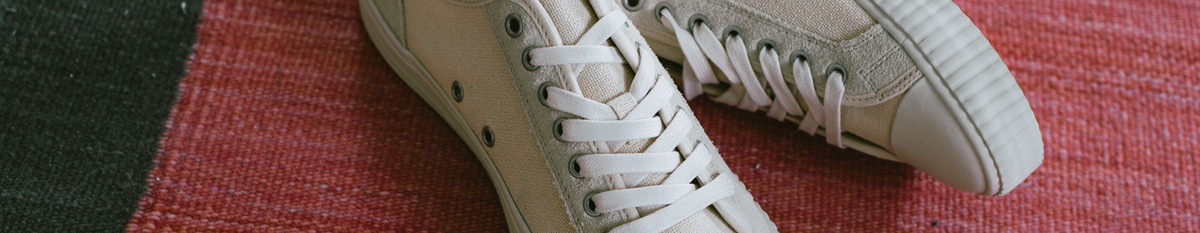 Close-up of beige low-top sneakers on a red rug.