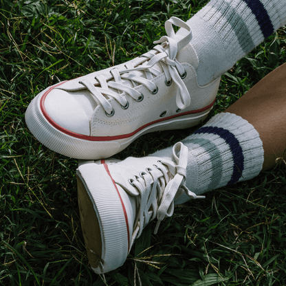 Close-up of white low-top sneakers with crimson accents, worn with white ankle socks on grass.