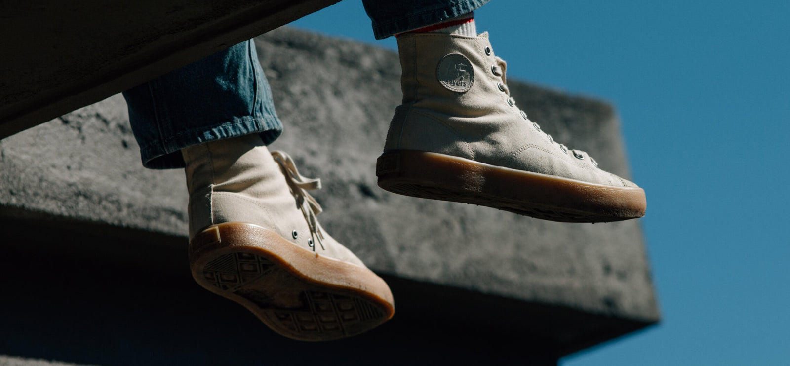 Person wearing beige high-top sneakers with tan soles on a concrete surface against a blue sky.