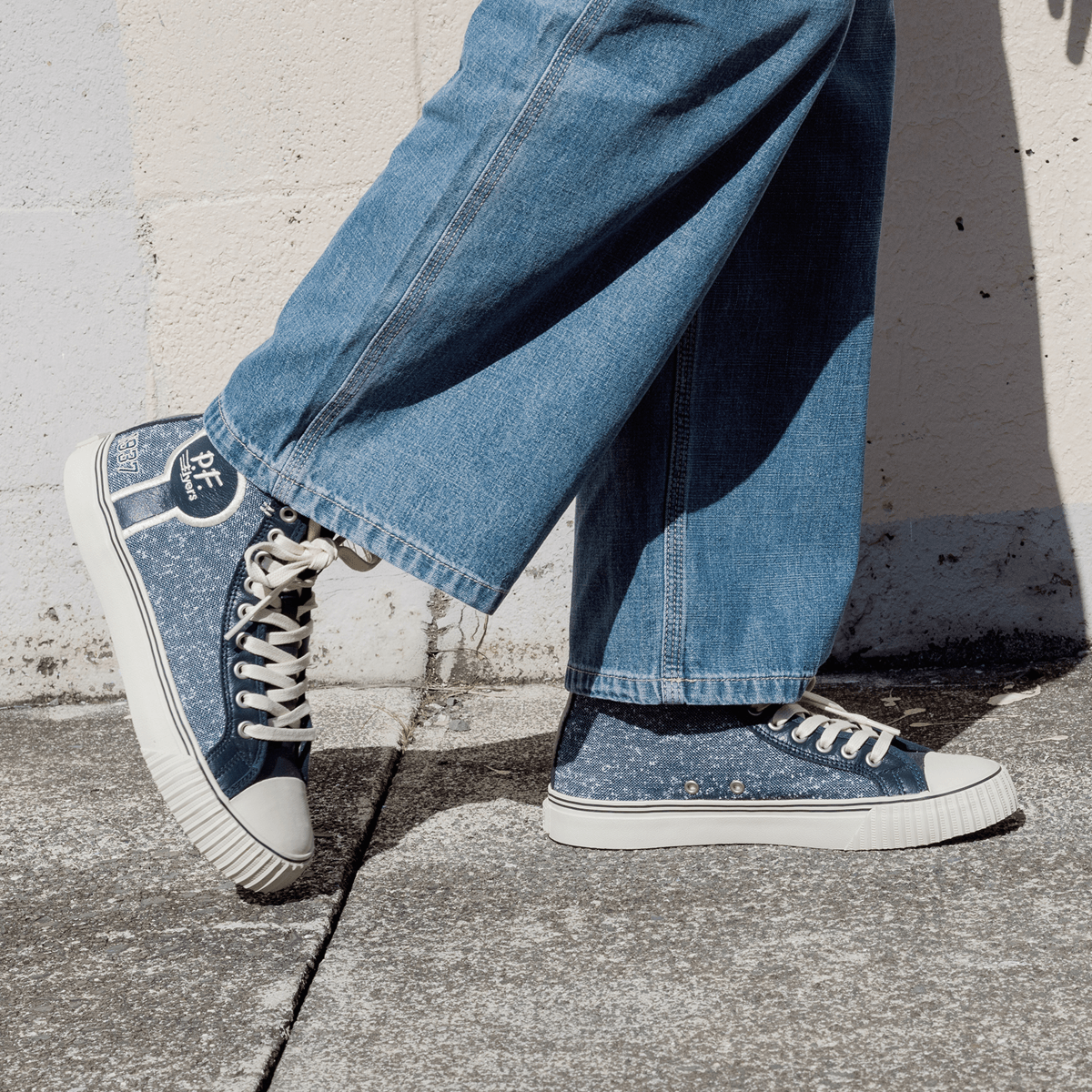 Navy jersey-textured high-top sneakers worn with blue jeans, standing against a concrete wall.