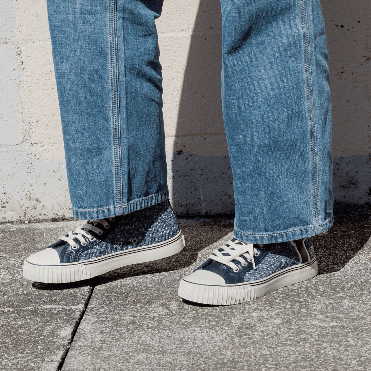 Navy jersey-textured high-top sneakers worn with jeans, standing against a concrete wall.