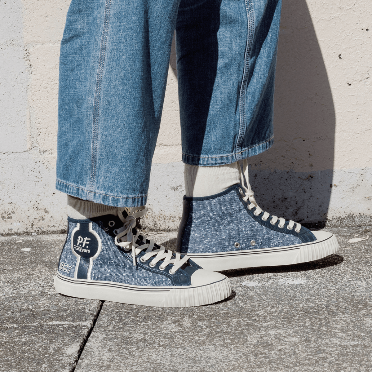 Navy jersey-textured high-top sneakers worn with jeans, standing against a concrete wall.