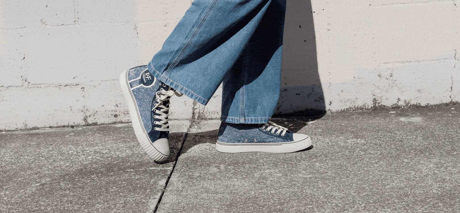 Two pairs of legs wearing navy jersey-textured sneakers with white soles standing on a sidewalk.