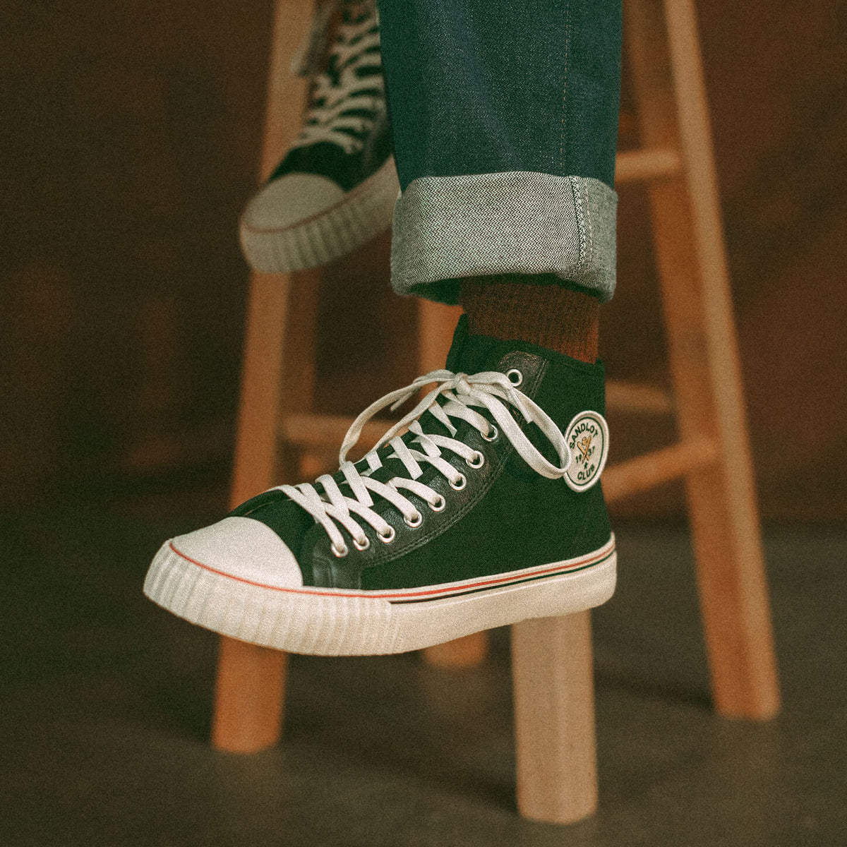 Black high-top sneakers with white soles worn by a person on a wooden stool.