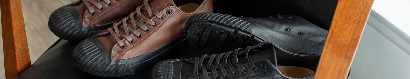 Pair of brown and black low-top leather sneakers on a chair.