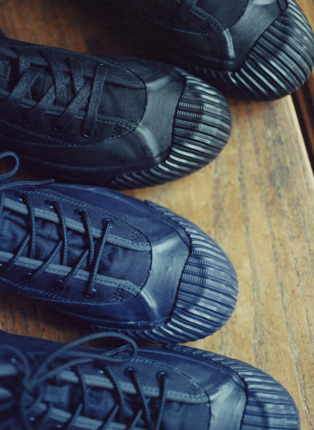 Two pairs of dark canvas boots with lugged rubber outsoles resting on a wooden surface.