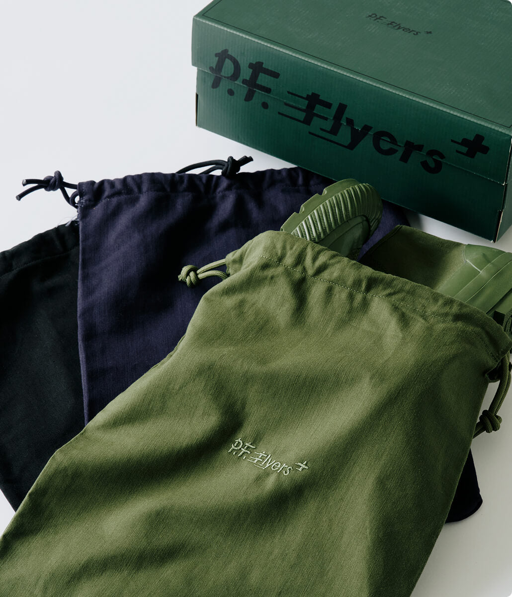 An olive green boot in a matching drawstring pouch, with a navy drawstring pouch and dark green shoe box in the background.