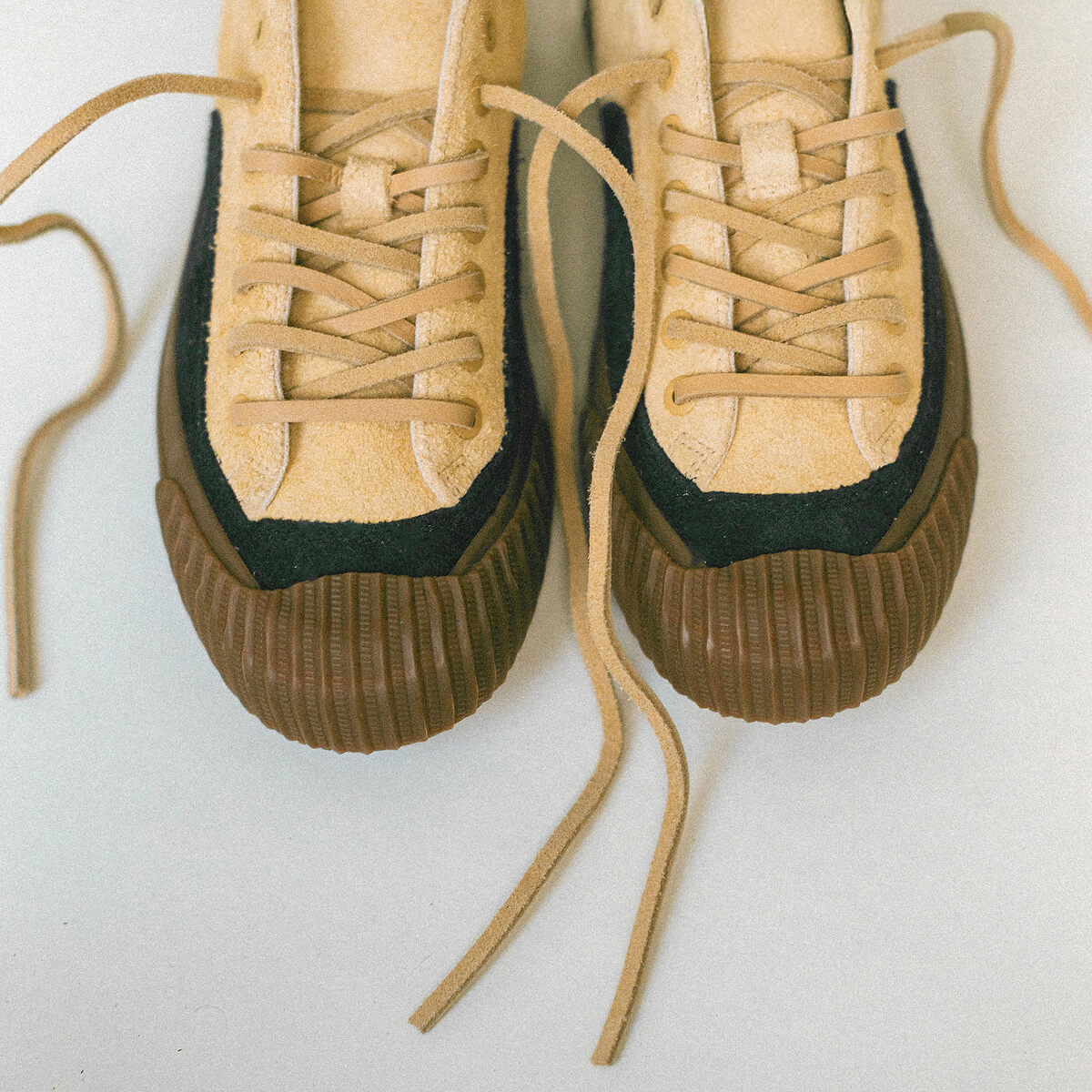 Pair of suede tan sneakers with black soles on a light background