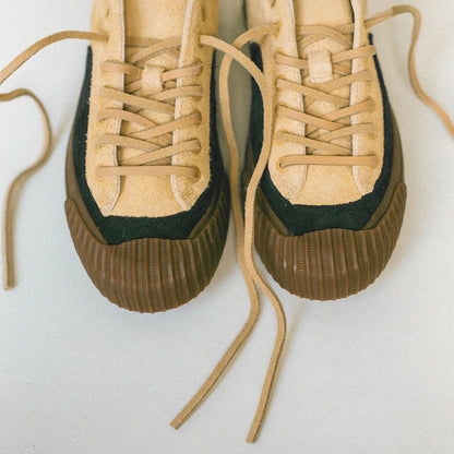 Pair of suede tan sneakers with black soles on a light background