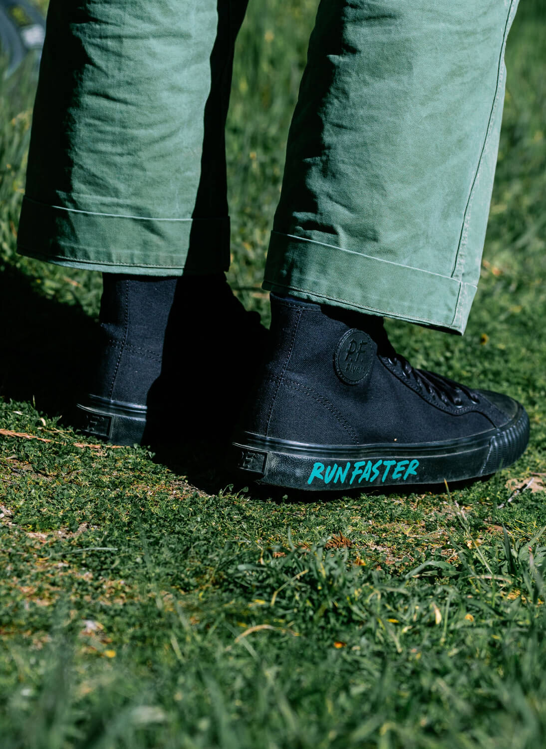 Close-up of a person wearing black canvas high-top sneakers with 'RUN FASTER' printed on the midsole.