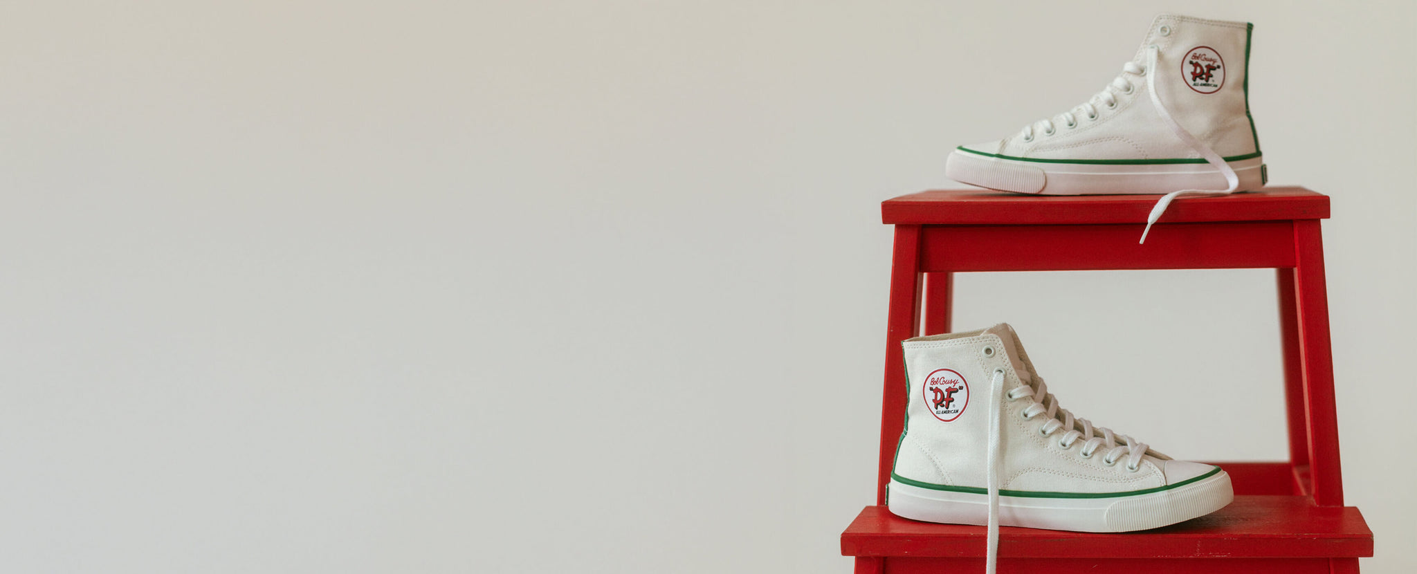 White high-top sneakers with green accents on a red stool against a white background