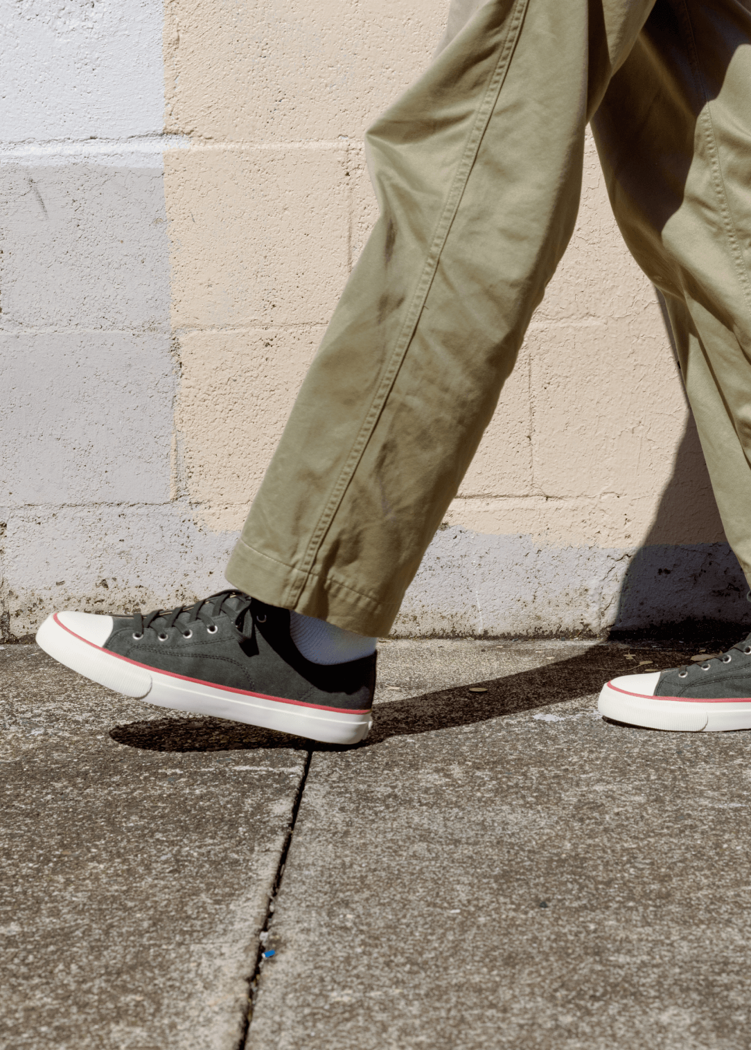 Person wearing khaki pants and black sneakers on a sidewalk.