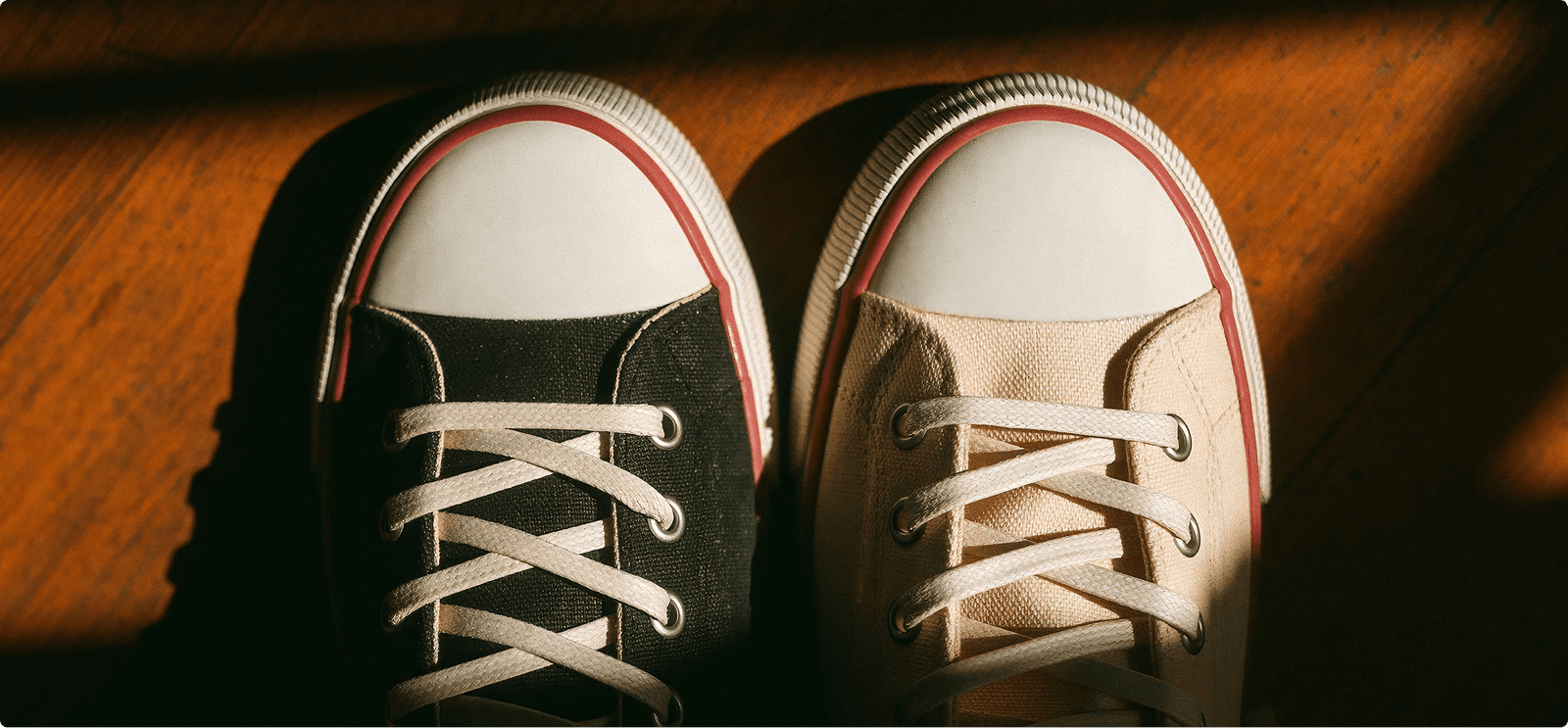 Close-up of a black and an off-white sneaker paired on a wooden floor.
